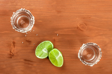 A photo of two tequila shots with lime wedges, shot from above on a rustic background with a place for text