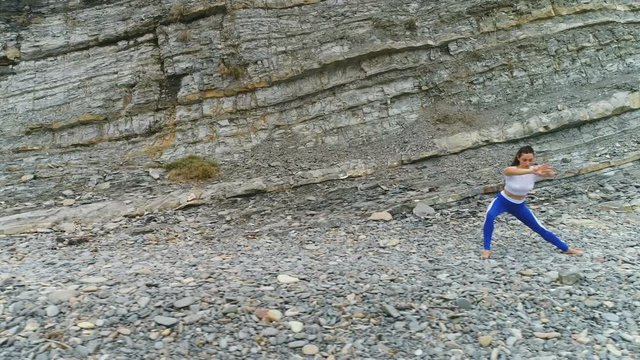 Woman is doing squats the bodyflex during breathing exercises on the rock background. Aerial beautiful footage view.