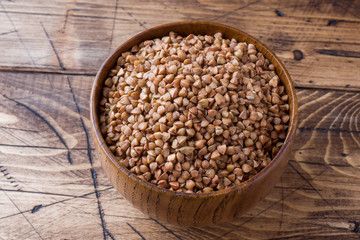 Buckwheat raw in a wooden bowl on a rustic wooden background.