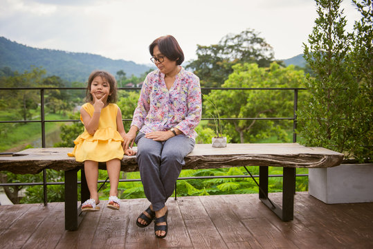 Happy grandmother with granddaughter sitting on a bench in summer park. Happy senior lady playing with little girl in outdoors cafe.