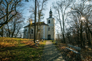 Church of Saint Johannes Nepomuk built in 18th century, standing on a hill at Mala Chuchle, Czech Republic, Europe, sunny autumn park, trees, green grass, leaves, pavement, benches, sunlight, blue sky