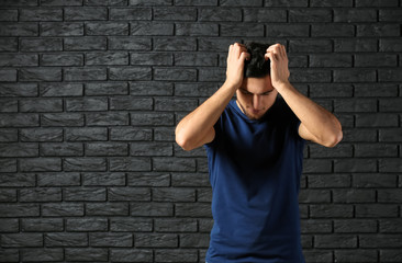 Emotional young man after making mistake against dark brick wall