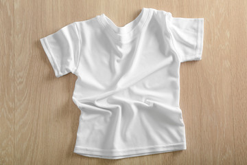 White t-shirt on wooden background, top view