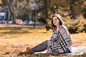 Beautiful young woman sitting on plaid in autumn park