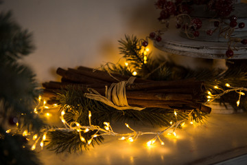 Long sticks of cinnamon tied with a rope, lit Christmas garland, lie among the fir branches. The comfort of home, a festive Christmas atmosphere, decor items new year