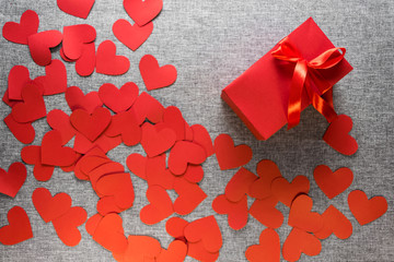 The gift box is wrapped in a red ribbon, and with paper hearts around, on a gray background