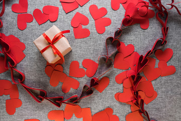The gift box is wrapped in a red ribbon, and with paper hearts around, on a gray background