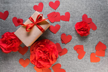 the gift box is wrapped in a red ribbon, and with paper hearts and flowers around, on a gray background