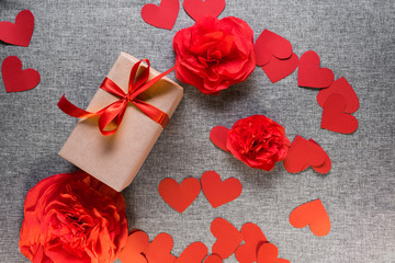 the gift box is wrapped in a red ribbon, and with paper hearts and flowers around, on a gray background