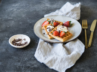 Belgian waffles with milk cream, chocolate and strawberries on a gray plate on a dark gray background