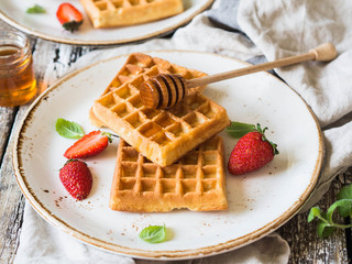 Belgian waffles with honey and strawberries on a white plate on a wooden rustic background