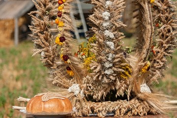 Tradycyjny wieniec dożynkowy z położonym obok chlebem i wplecionymi kwiatami.