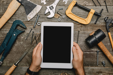 Partial view of man using digital table with blank screen on wooden background with different tools