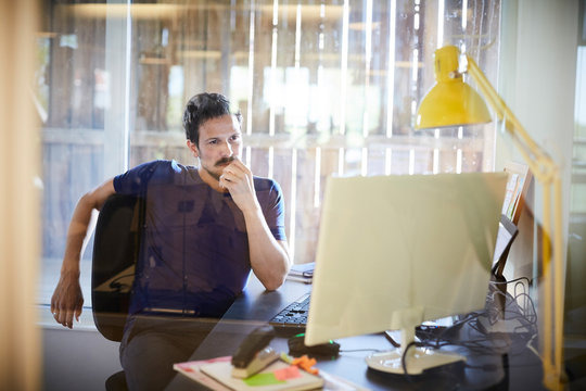 Creative businessman looking at computer monitor while sitting in office