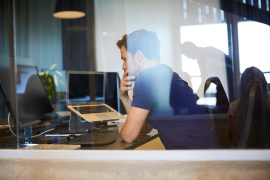 Businessman sitting at computer desk seen through glass in office