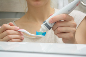 Woman hand holding a toothbrush with a toothpaste applied on it in the bathroom. Close up of female hand ready for brushing teeth. Young woman hand holding a pink toothbrush with white tooth paste.