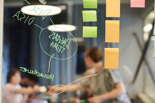 Text and sticky notes on glass with business people in background at office