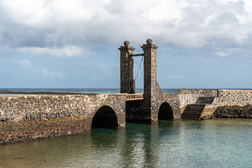 Sea landscape with an old stone bridge and a gate. Puente de las Bolas (Balls Bridge), landmark of Arrecife, the capital of Lanzarote, Spain.