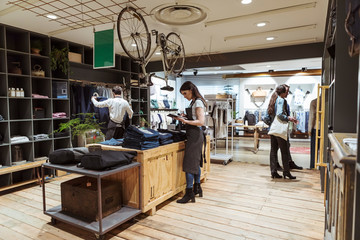 Colleagues analyzing purchase order while customers shopping at boutique