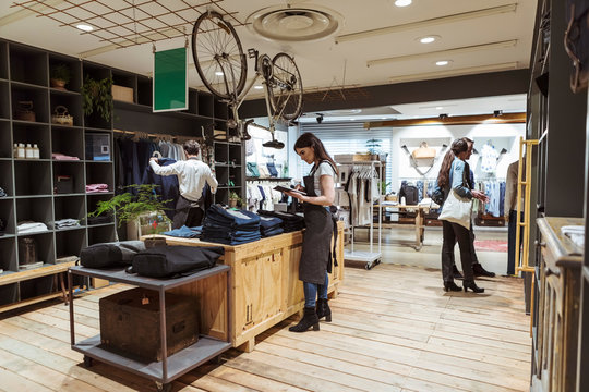 Colleagues analyzing purchase order while customers shopping at boutique