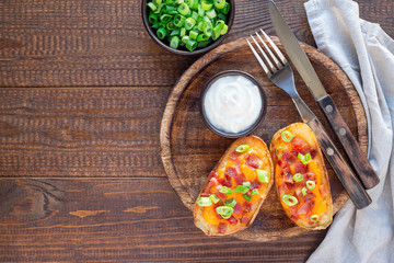 Baked loaded potato skins with cheddar cheese and bacon on a wooden plate, garnished with scallions and sour cream, horizontal, top view, copy space