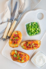 Baked loaded potato skins with cheddar cheese and bacon on ceramic plate, garnished with scallions and sour cream, vertical, top view