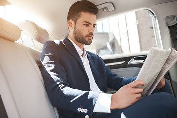 Young stylish businessman reads newspaper on backseat of car