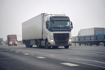 Carriage of goods by road, trucking industry - Semi-trailer truck driving trough the fog and haze. Smoke on the road. Foggy gray road, cars and trucks driving fading into thick fog. Low visibility.