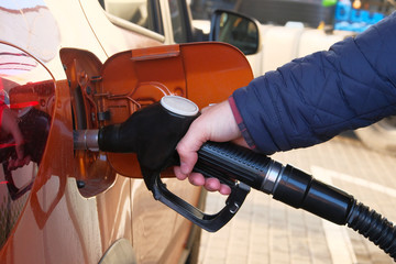 Man fills up his orange car with a gasoline at gas station. Gas station pump. To fill car with diesel fuel.