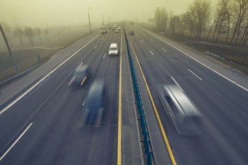 Сars in motion driving in the fog and mist. Bad driving conditions. Dangerous situation on the road. Foggy gray road, cars and trucks driving fading into the thick fog. Low visibility. Smoke on road
