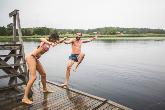 Full length of playful woman pushing male friend in lake while standing on jetty during weekend getaway