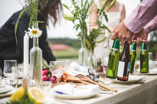 Cropped image of man holding beer bottles at dining table during dinner party in backyard