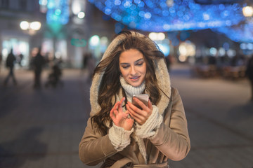 Woman using smart phone for texting while standing in the street.