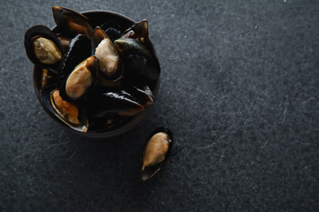 Fresh mussels in black ceramic bowl on dark concrete background. Overhead view, copy space.
