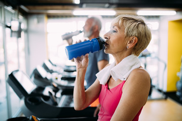 Fototapeta na wymiar Senior woman drinking bottle of water on threadmill in gym