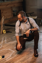 Serious male detective sitting at crime scene and looking on chalk line