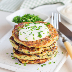 Vegetarian zucchini fritters or pancakes, served with greek yogurt and green onion on a ceramic plate, square format