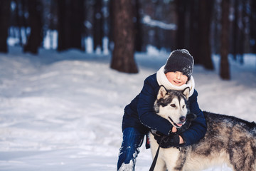 A cheerful European teenager hugs a big dog in the winter in the forest. The concept of winter holidays