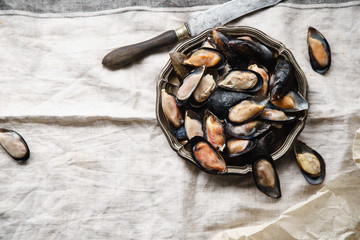 Frozen mussels in metallic vintage plate on linen tablecloth with stripes. Overhead view with text space