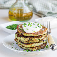 Vegetarian zucchini fritters or pancakes, served with greek yogurt and green onion on a white plate, square format