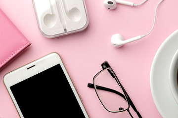 White smartphone and a cup of coffee and office supplies on a bright pink background. view from above