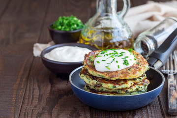 Obraz na płótnie Canvas Vegetarian zucchini fritters or pancakes, served with greek yogurt and green onion, in little pan, horizontal, copy space