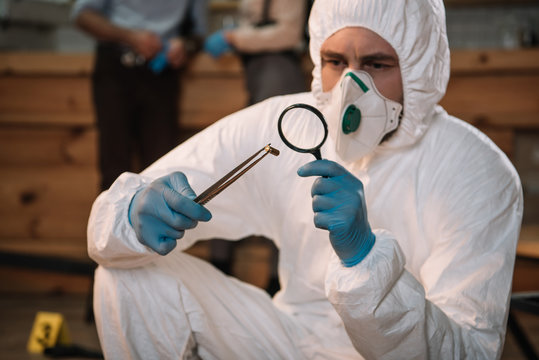 Close Up Of Forensic Investigator Examining Evidence With Magnifying Glass At Crime Scene