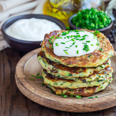 Vegetarian zucchini fritters or pancakes, served with greek yogurt and green onion on a wooden plate, square