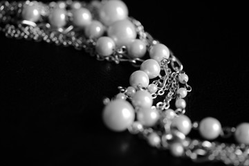 Necklace of white beads and metal chain on a dark background close up. Black and white