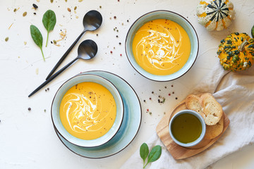Orange pumpkin soup in plates with cream and olive oil on white background. Top view
