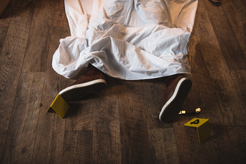 cropped legs of dead dead body covered with white sheet at crime scene