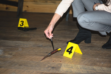 cropped view of female hand examining knife near evidence markers at crime scene