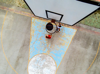 Top view of two young friends playing basketball on court outdoors.