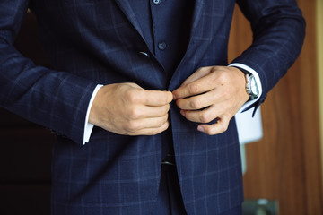 Close-up business stylish man buttoning his jacket, standing in a stylish office with designer repair.